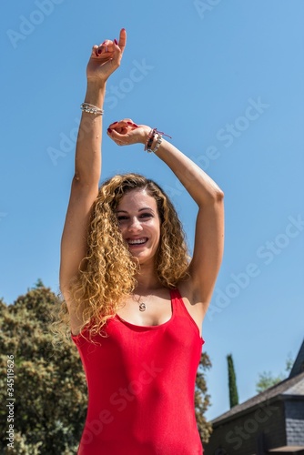 Blonde girl with curly hair and a red swimsuit gesticulating with her hand raised while smiling