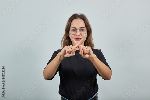 Cute Young Brunette Woman In Black T-Shirt  Blue Jeans With Belt On Gray Background  Upset Girl Protests And Crosses Her Index Fingers In Disagreement
