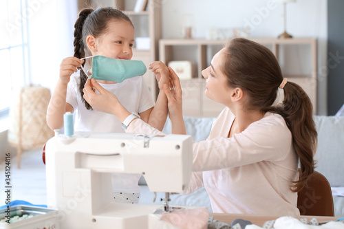 Little daughter with her mother sewing protective masks at home