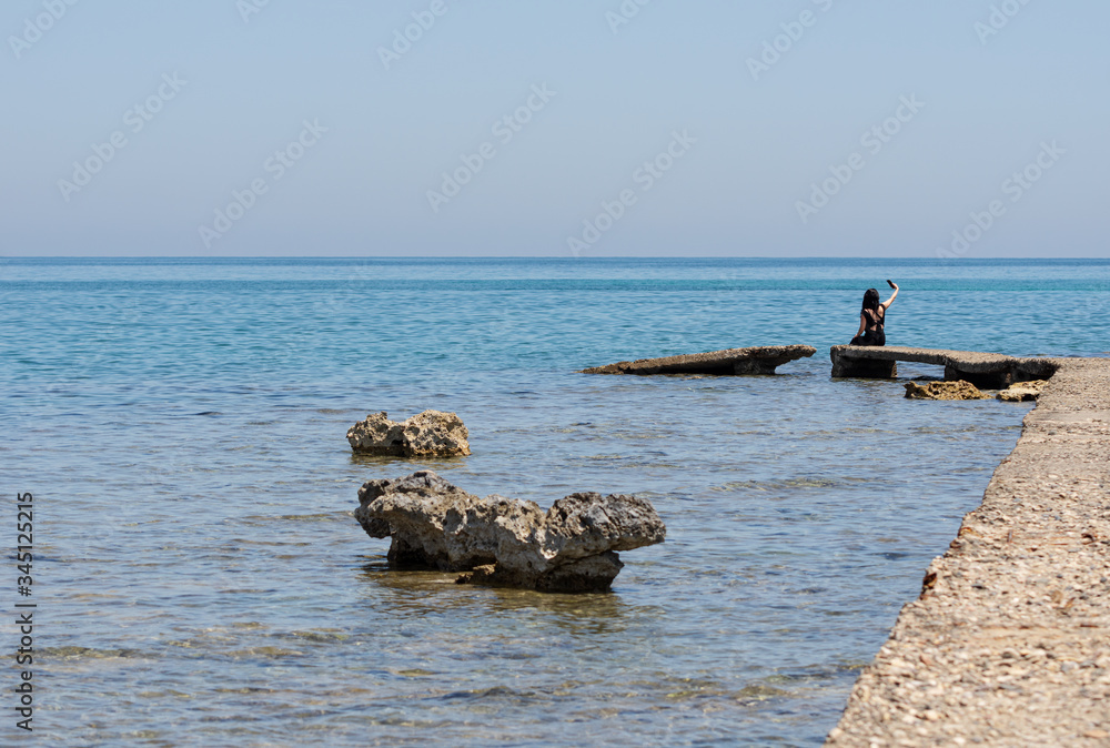Fototapeta premium A woman sitting on the rock looking sea and taking photo