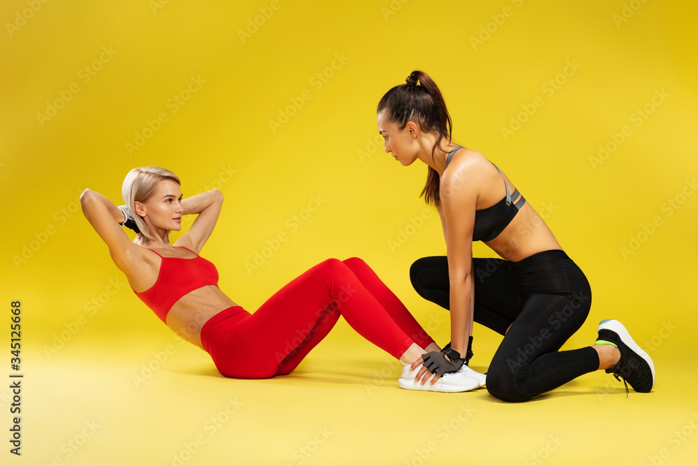Fitness exercises. Attractive sporty blonde woman in red sportswear pumping press, exercising with personal trainer against yellow bakground Fitness exercises. Attractive sporty blonde woman in red sportswear pumping press, exercising with personal trainer against yellow bakground