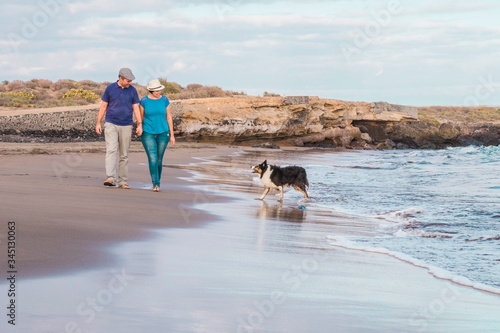 Adult couple in love walk outdooor holding hands and enjoying their nice beautful pet dog at the beach - concept of end lockdown phase for coronavirus emergency photo