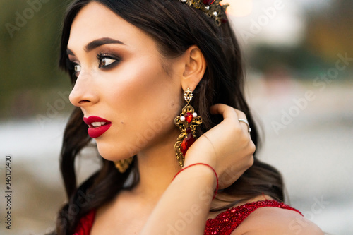 Beautiful brunette in a red dress with a crown. A brunette girl with smile. Background wildlife,sunlight, lush grass. Artistic photo. Wedding photosoot photo