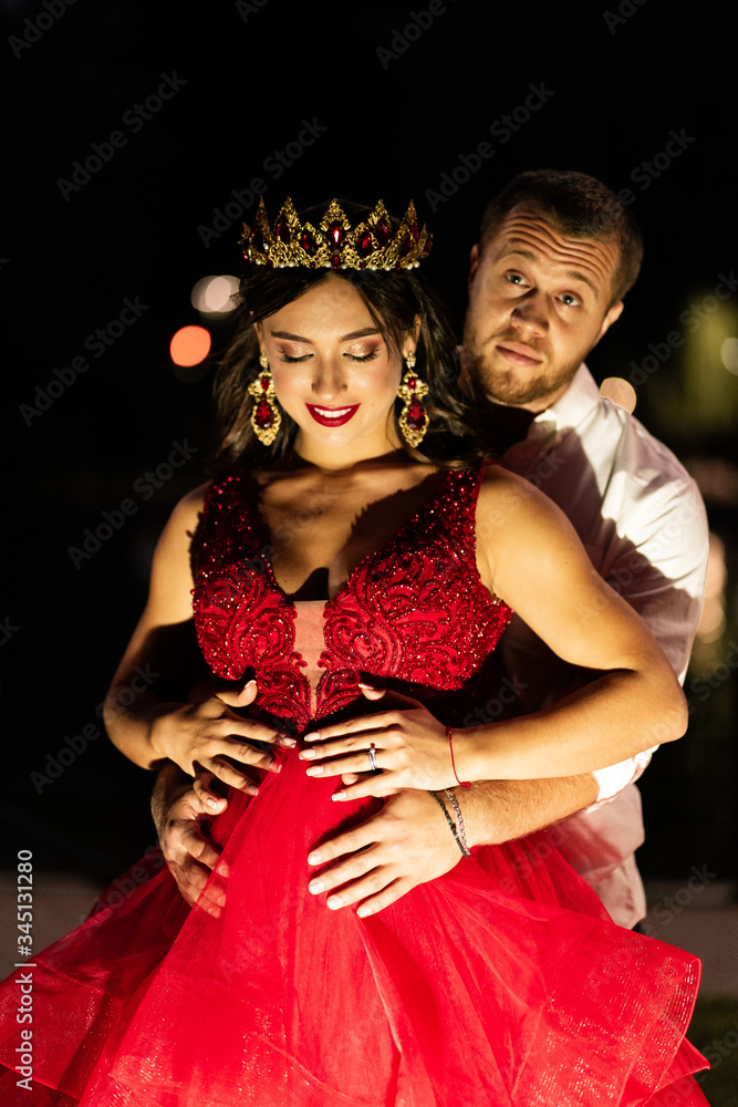 Beautiful romantic couple. Attractive young woman in red dress and crown with handsome man in white shirt are in love on night time outdoor. Happy Saint Valentine's Day. Pregnant and wedding concept. Beautiful romantic couple. Attractive young woman in red dress and crown with handsome man in white shirt are in love on night time outdoor. Happy Saint Valentine's Day. Pregnant and wedding concept.