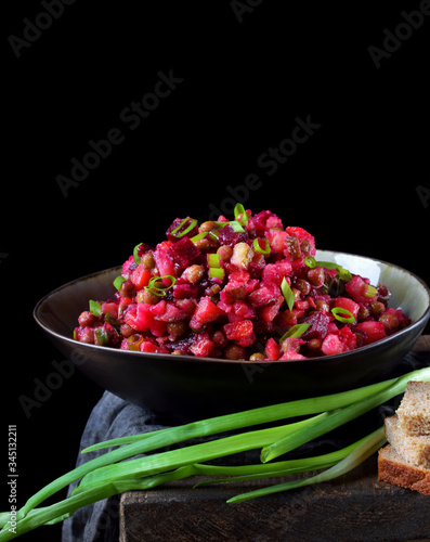 Vinaigrette salad with boiled vegetables in a clay bowl against the black background. Russian cuisine meal