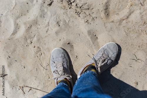 Walk along the beach. A man stands in the sand, dressed in jeans and sneakers.