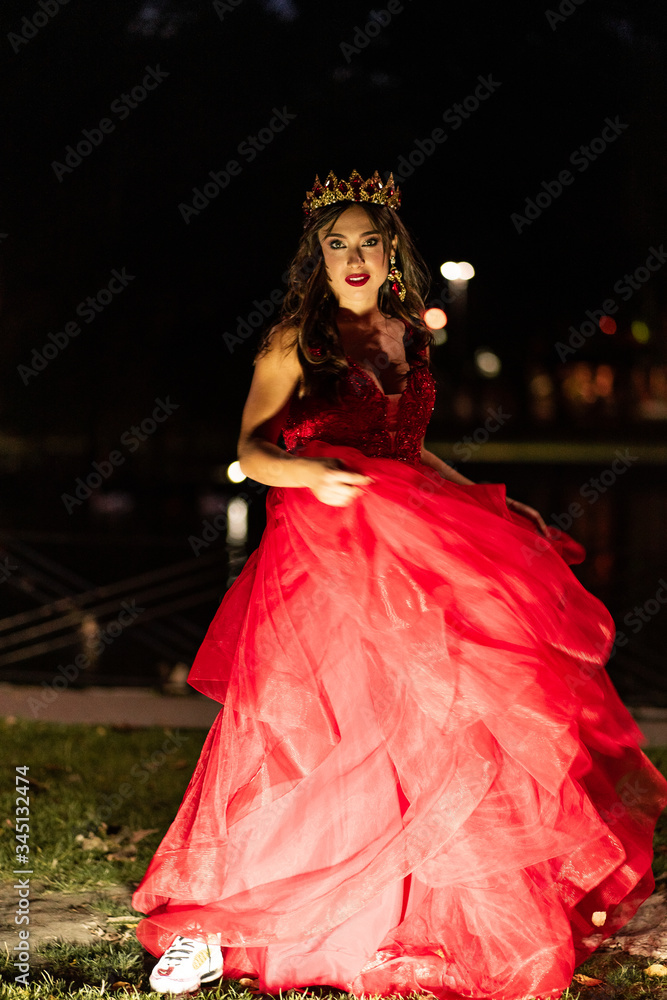 Fototapeta premium Beautiful brunette in a red dress with a crown. A brunette girl dancing on night time. Artistic photo. Wedding or pregnant photosoot