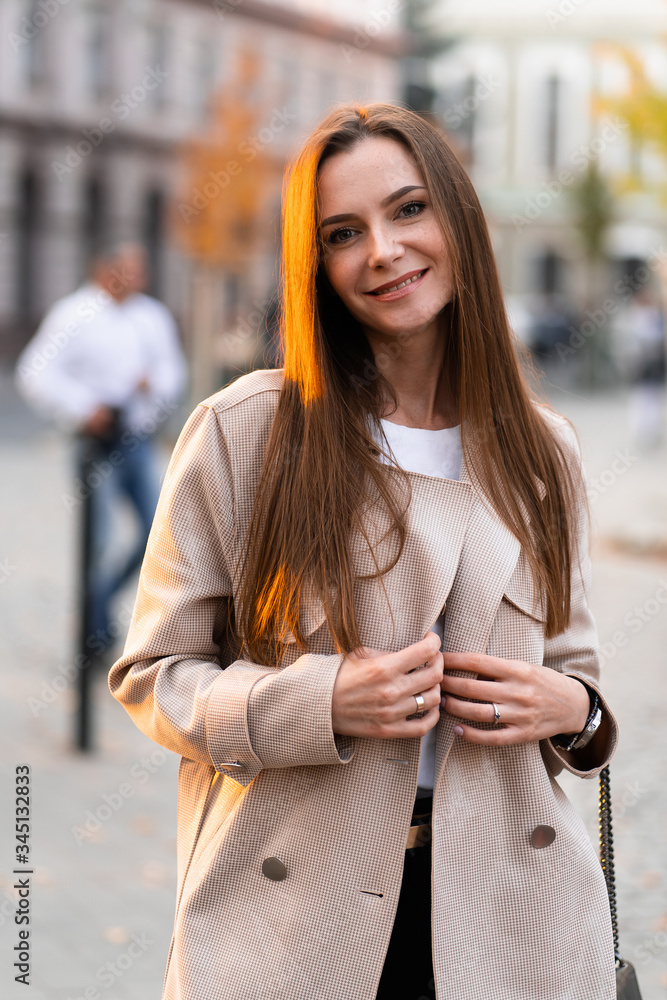 Outdoor photo of brunette lady walking on street background in autumn day.Fashion street style portrait. wearing dark casual trousers, white sweater and creamy coat.Fashion concept.