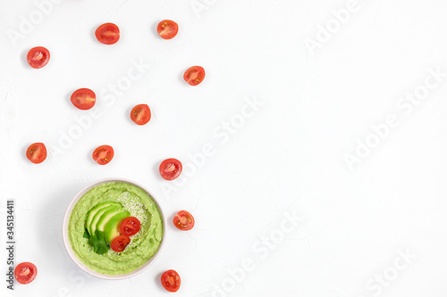 hummus consisting of avocados and green peas, chickpeas in bowls. on a white background decorated with tomatoes. copy space. flat lay. oriental dish appetizer