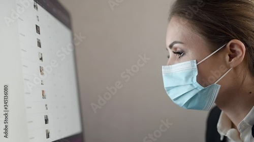 Work during self-isolation and quarantine. Side view of young woman employee in a medical facial mask works in the office at the computer. Coronavirus Pandemic Covid 19.