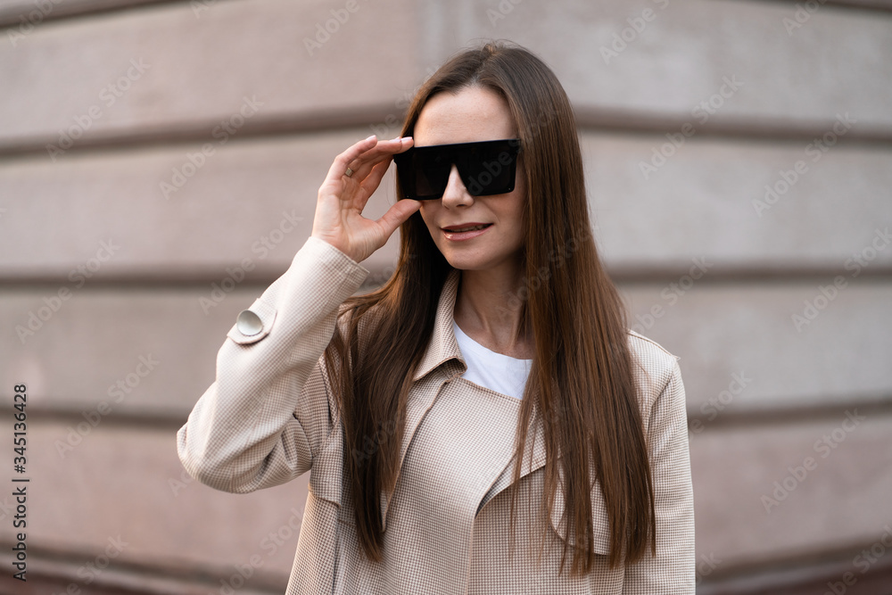 Beautiful brunette woman wearing sunglasses walking on street.Stylish smiling business woman wearing dark casual trousers, white sweater,creamy coat and sunglasses .Fashion concept. Beautiful brunette woman wearing sunglasses walking on street.Stylish smiling business woman wearing dark casual trousers, white sweater,creamy coat and sunglasses .Fashion concept.