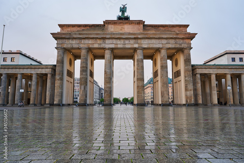 berlin germany, deserted brandenburg gate with reflections on the wet asphalt and with clouds. special perspective as close-up from the ground, tv tower and town hall in the background