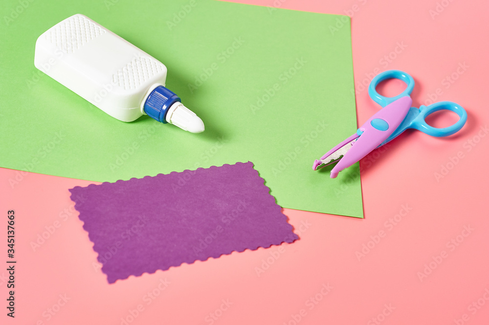 Scissors for decorative curly cutting, glue bottle and blank paper sheets for craft with wave border on pink background. Concept of handmade, leisure or preschool education