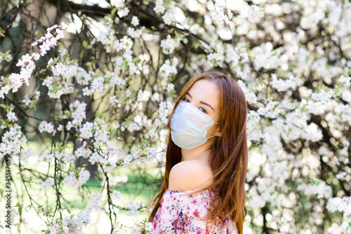 Girl, young woman in a protective sterile medical mask on her face in the spring garden. Air pollution, virus, pandemic coronavirus concept.