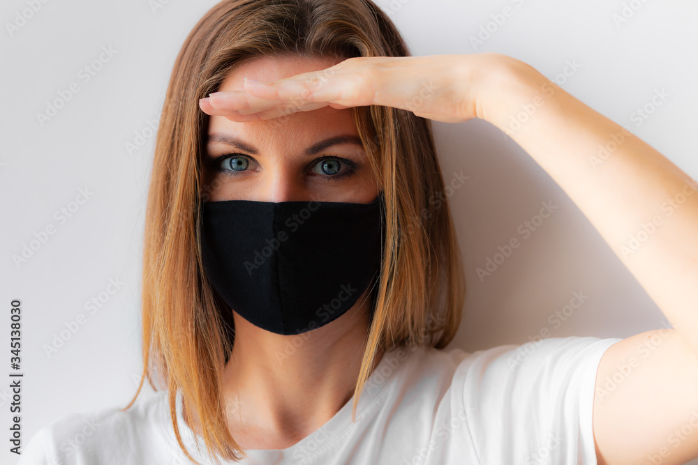 Beautiful close-up portrait of a young woman in a black medical mask and white T-shirt on white background, with hand near forehead. Quarantine, coronavirus epidemic pandemic, covid-19. Stay home. Beautiful close-up portrait of a young woman in a black medical mask and white T-shirt on white background, with hand near forehead. Quarantine, coronavirus epidemic pandemic, covid-19. Stay home.