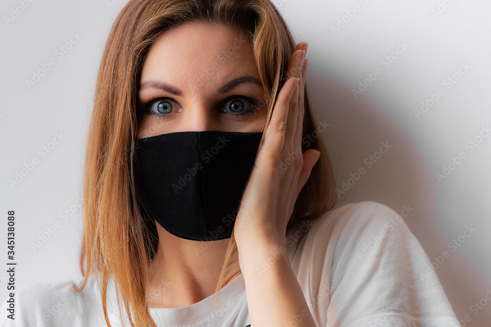 Close-up portrait of a young shocked woman in a black medical mask and white T-shirt on white background, with hand near head. Quarantine of coronavirus epidemic just ended, covid-19. Stay home. Close-up portrait of a young shocked woman in a black medical mask and white T-shirt on white background, with hand near head. Quarantine of coronavirus epidemic just ended, covid-19. Stay home.