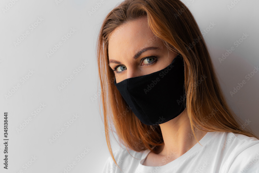 Close-up portrait of a young woman in a black medical mask and white T-shirt on white background. Quarantine, coronavirus epidemic pandemic, covid-19. Stay home concept. Virus protection. . Close-up portrait of a young woman in a black medical mask and white T-shirt on white background. Quarantine, coronavirus epidemic pandemic, covid-19. Stay home concept. Virus protection. .