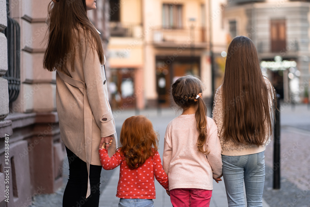 Happy family. mother of many children and three daughters child girl together, walking and joyfully laughing while relaxing on park on a summer holiday. Family outdoors lifestyle. Back view