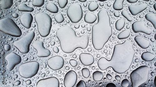 Large raindrops lying on a steel surface in a monochrome color.
