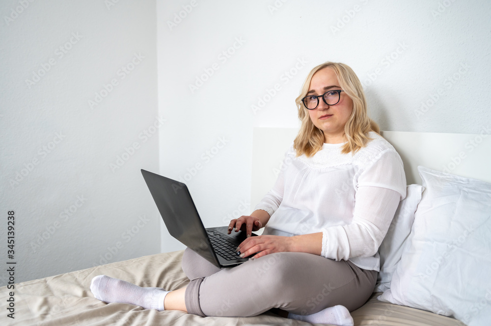 Blond woman in glasses working at home on sofa using laptop Blond woman in glasses working at home on sofa using laptop