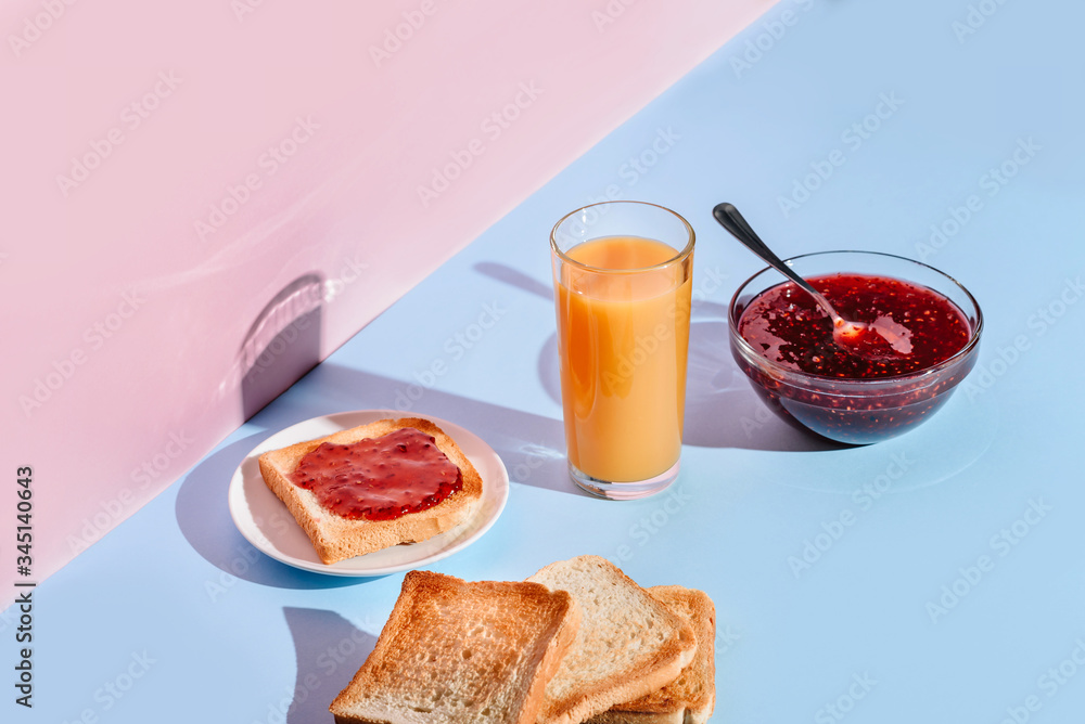 Breakfast with toast, jam and juice, lit by the sun on blue and pink backgrounds with a copy space. Breakfast with toast, jam and juice, lit by the sun on blue and pink backgrounds with a copy space.