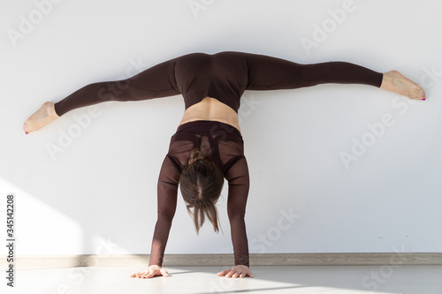 Fototapeta Naklejka Na Ścianę i Meble -  A girl in a tracksuit stands on her hands in a light yoga studio