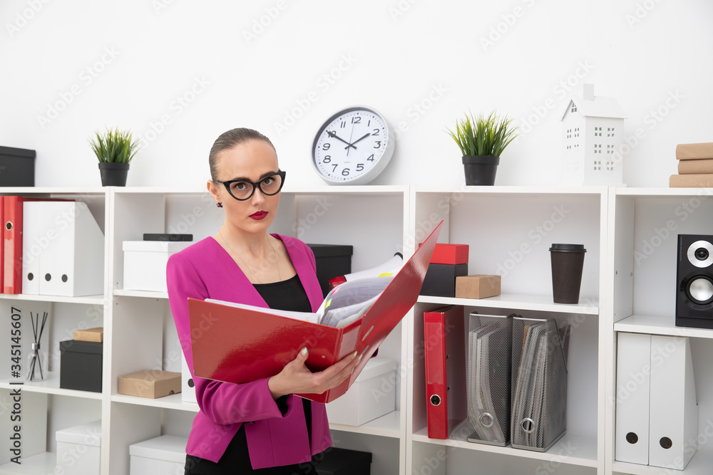 Portrait of a business-style girl looking for documents in a red folder. Office working day Portrait of a business-style girl looking for documents in a red folder. Office working day