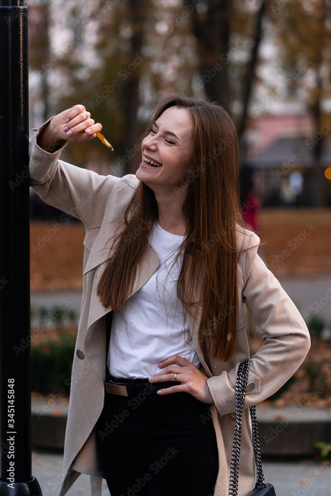 Outdoor fashion portrait of stylish young woman having fun, emotional face , laughing, Urban city street style wearing dark casual trousers, white sweater,creamy coat. and sunglasses Fashion concept.