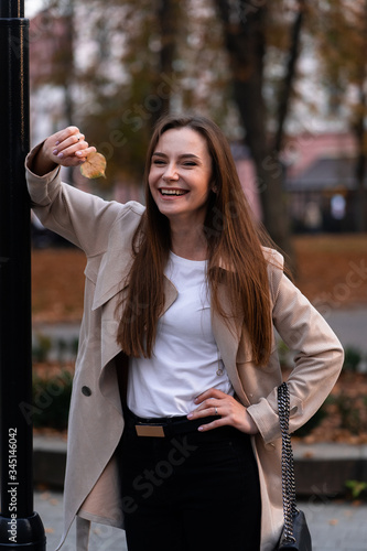 Outdoor fashion portrait of stylish young woman having fun, emotional face , laughing, Urban city street style wearing dark casual trousers, white sweater,creamy coat. and sunglasses Fashion concept.