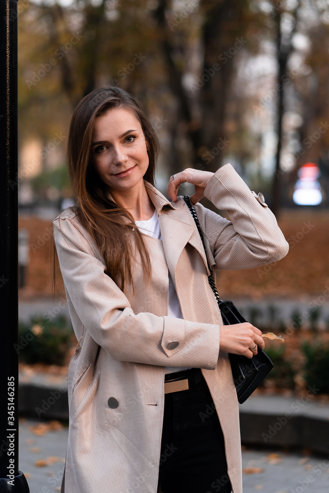 Outdoor fashion portrait of stylish young woman having fun, emotional face , laughing, Urban city street style wearing dark casual trousers, white sweater,creamy coat. and sunglasses Fashion concept.