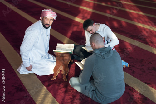 Group of muliethnic religious muslim young people praying and reading Koran together inside beautiful modern mosque. photo