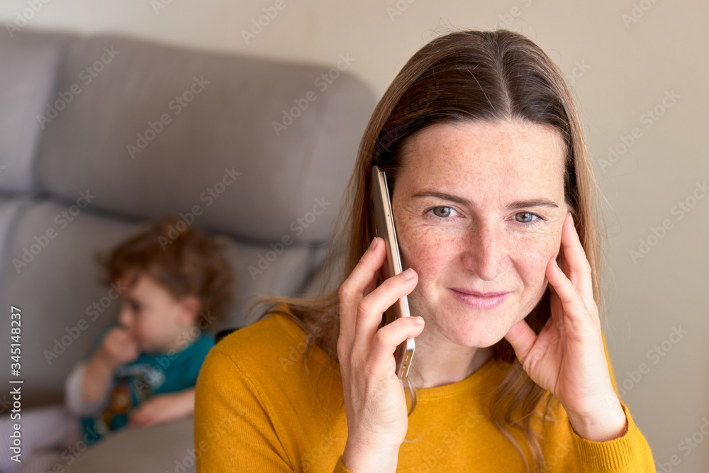 Woman talking on the phone at home with her son behind Woman talking on the phone at home with her son behind