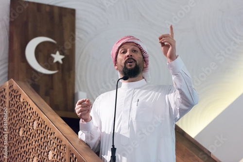 Muslims young arabic Imam has a speech on friday afternoon prayer in mosque. Muslims have gathered for the friday afternoon prayer in mosque and are listening to the speech of imam photo