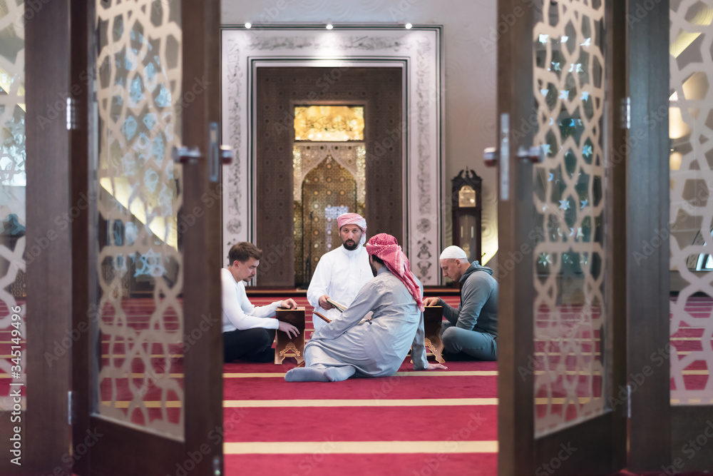 Group of muliethnic religious muslim young people praying and reading Koran together inside beautiful modern mosque.