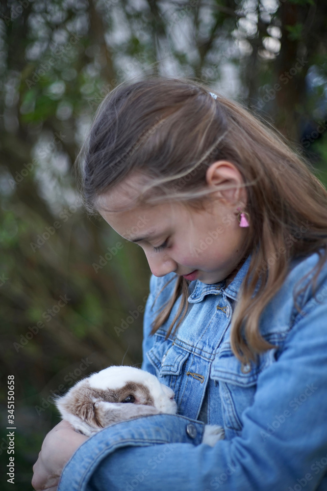 Portrait of a young blonde girl holding gently a pet bunny, rabbit in her arms outside in the garden. Portrait of a young blonde girl holding gently a pet bunny, rabbit in her arms outside in the garden.