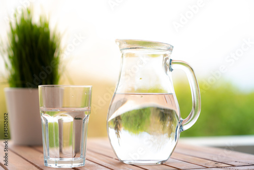 jug with water and a glass on a wooden table on the nature in the garden