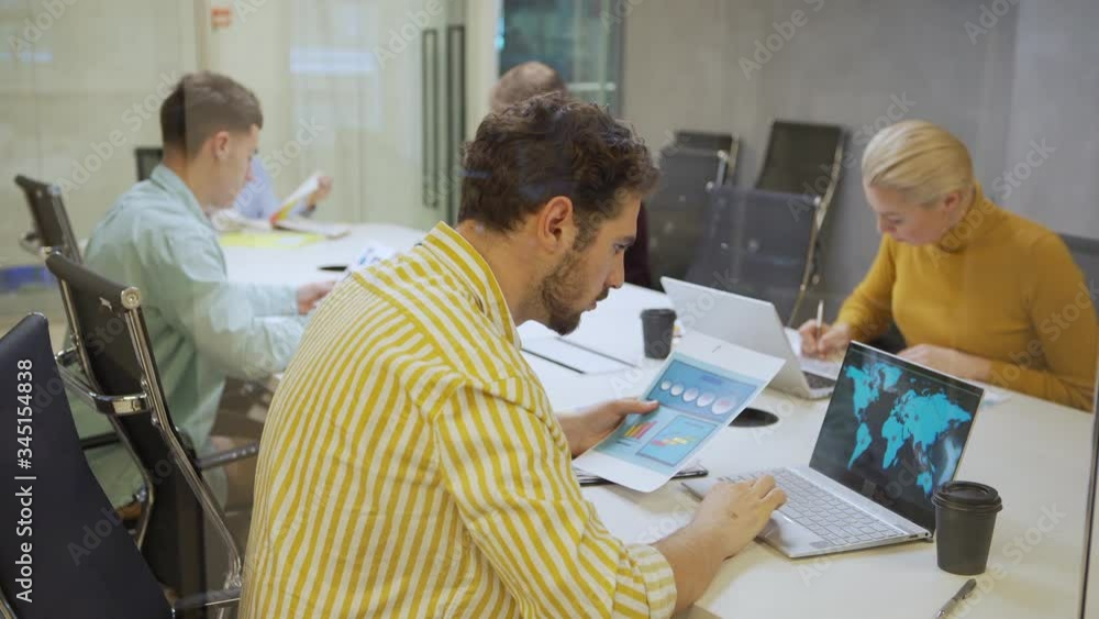 Panning medium shot of group of business analysts or market professionals working with data separately sitting at desk in office behind glass wall Panning medium shot of group of business analysts or market professionals working with data separately sitting at desk in office behind glass wall