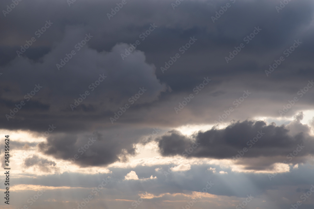 Dark clouds and sunshine rays in the sunset sky before a thunderstorm. Abstract contrasting background.