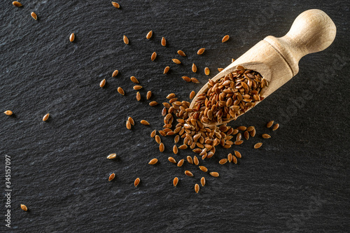 Fotografie Flax seed plant with brown linseed in wooden scoop for organic oil on dark stone