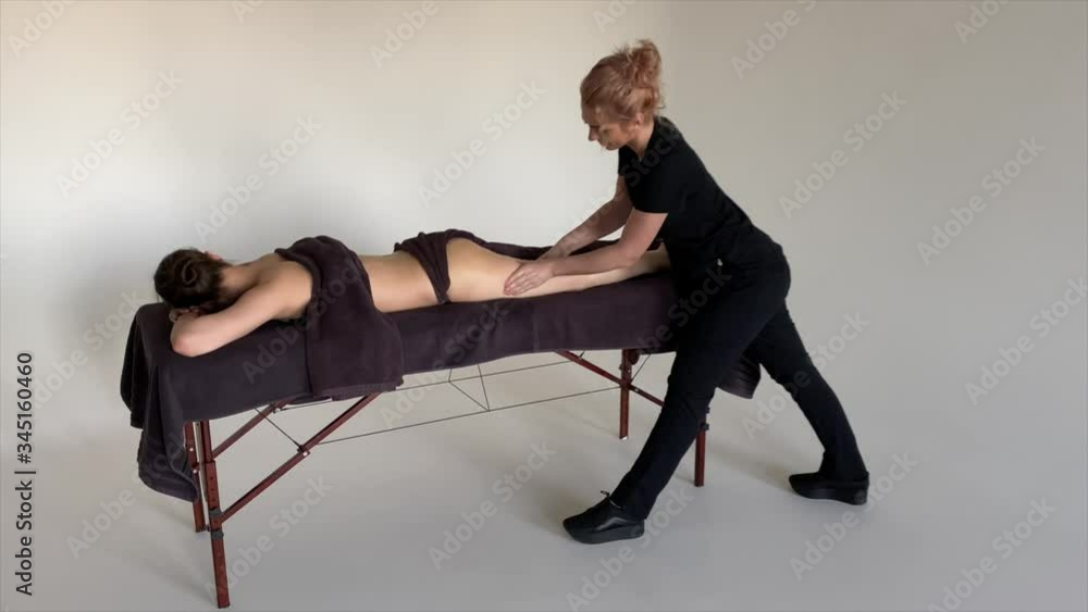 Funny fat burning massage. Portrait of cheerful woman masseur in uniforme near massage table with woman patient in wellness center. White background isolated Funny fat burning massage. Portrait of cheerful woman masseur in uniforme near massage table with woman patient in wellness center. White background isolated
