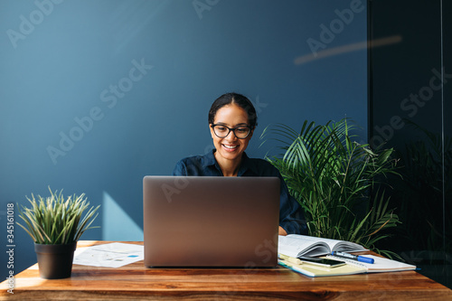 Smiling entrepreneur sitting at home working on laptop computer with documents on the table photo