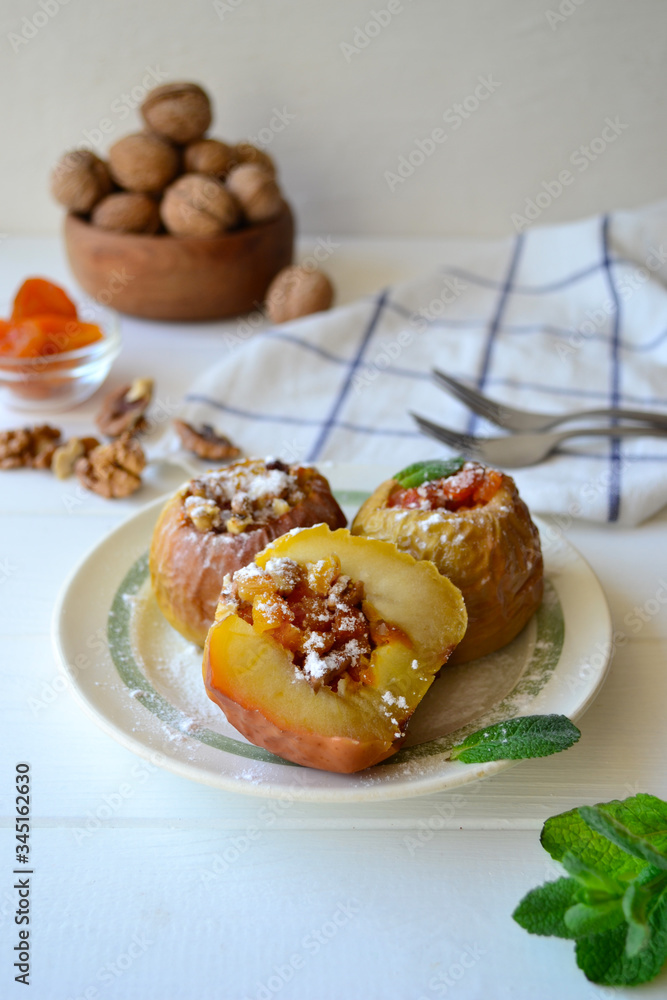 Baked apples filled with walnuts and dried apricots on a white wooden background.