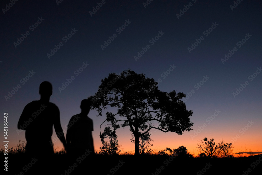 Men terkking and tree silhouette in bright colorful sunset day at Chapada dos Veadeiros National Park, nature reserve conservancy area of cerrado vegetation, Goiás, Brazil, South America. 