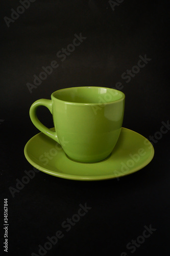 Green cup of coffee and saucer on a black background.
