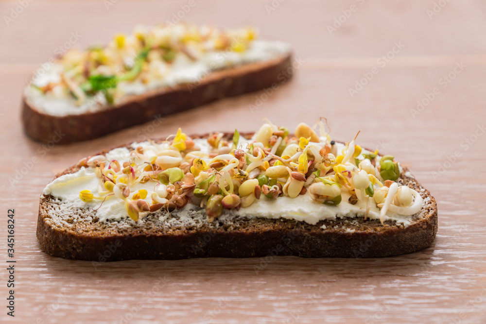 close up of rye bread sandwiches with cream cheese and sprouted mung beans, walnut, sunflower and flax on wooden background. vegan, raw food diet