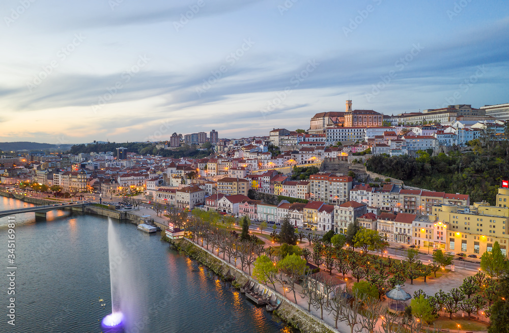 Coimbra drone aerial city view at sunset with colorful fountain in Mondego river and beautiful historic buildings, in Portugal