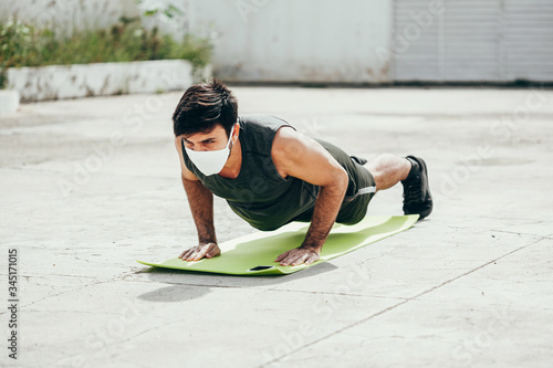 Young man working out outdoors wearing protective mask. Covid-19 and coronavirus concept