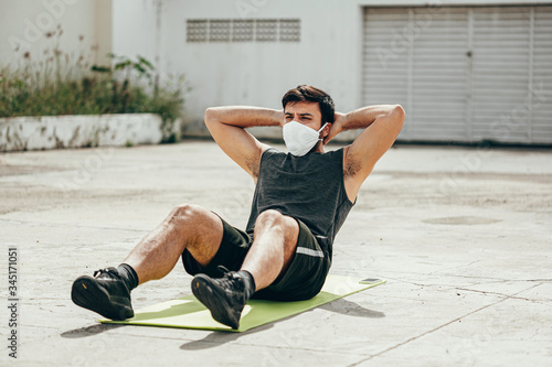 Young man working out outdoors wearing protective mask. Covid-19 and coronavirus concept