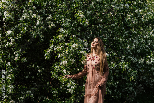 beautiful girl in a dress basks in the sun against a background of white flowers in a flowering garden