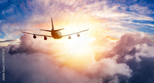 Aerial View of Commercial Airliner Jet Plane Flying in above the clouds during a colorful sunset or sunrise. Artistic Composite. Heavenly Sunlight. Nature Background